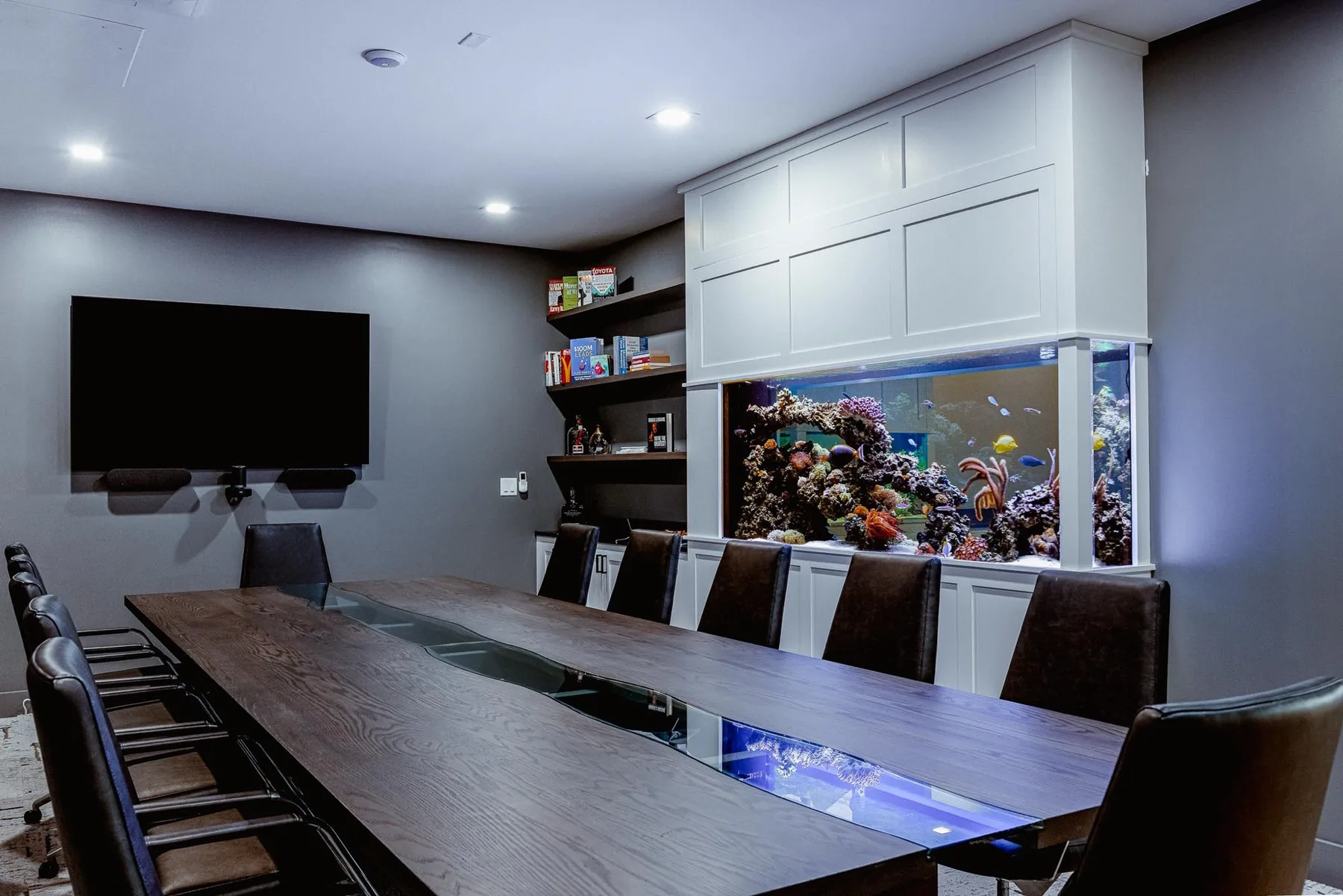 A long boardroom table facing a reef aquarium built into white cabinetry.